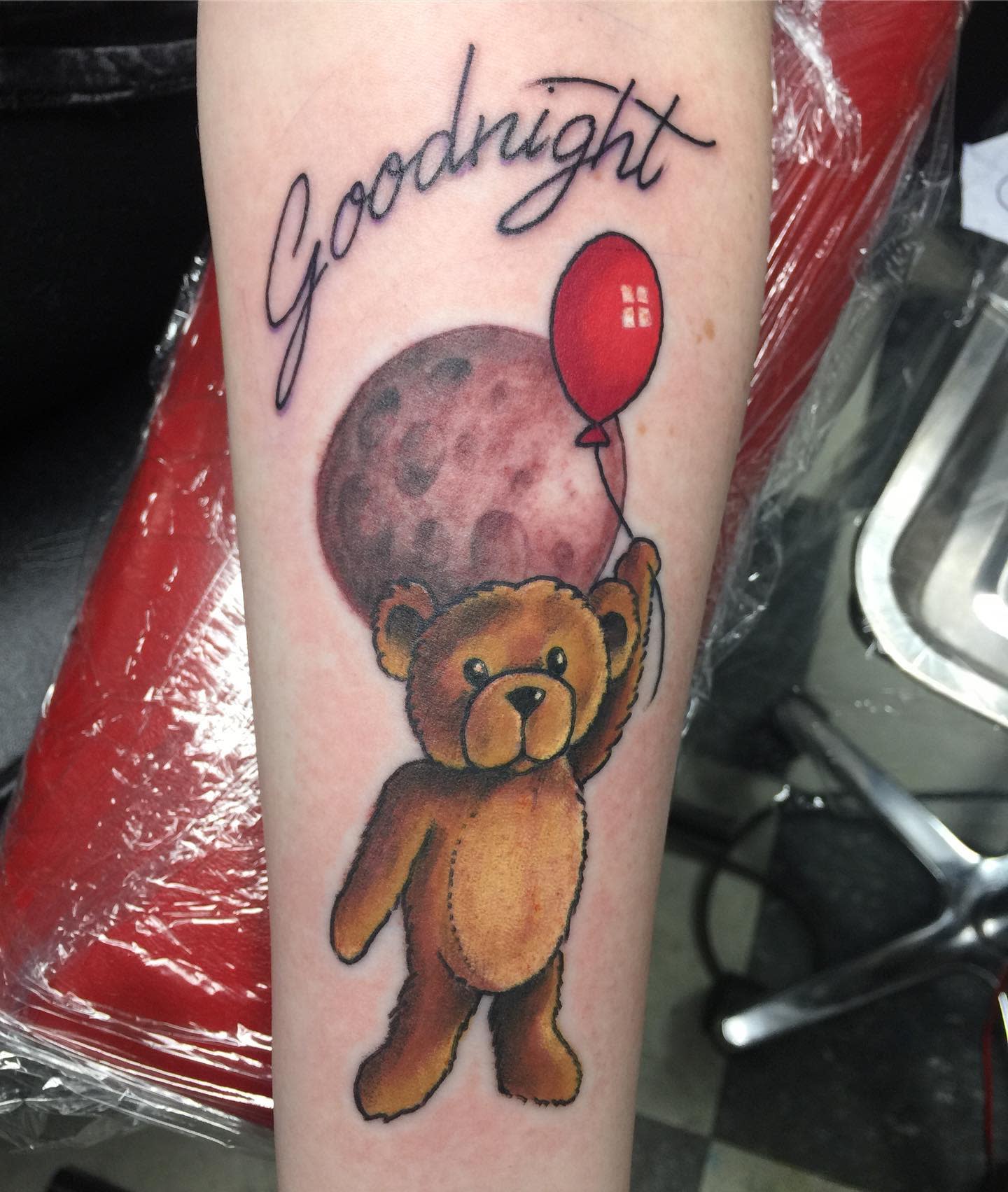 Tattoo of a teddy bear with a red balloon and "Goodnight" text, with a moon background